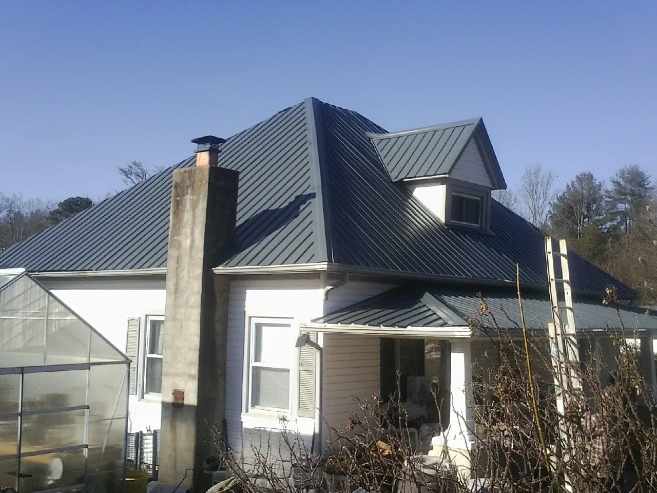 Dark blue standing seam metal roof on a white farmhouse with dormer — Slate & Tile Roof Repair by Roofing Brothers in Westerlo