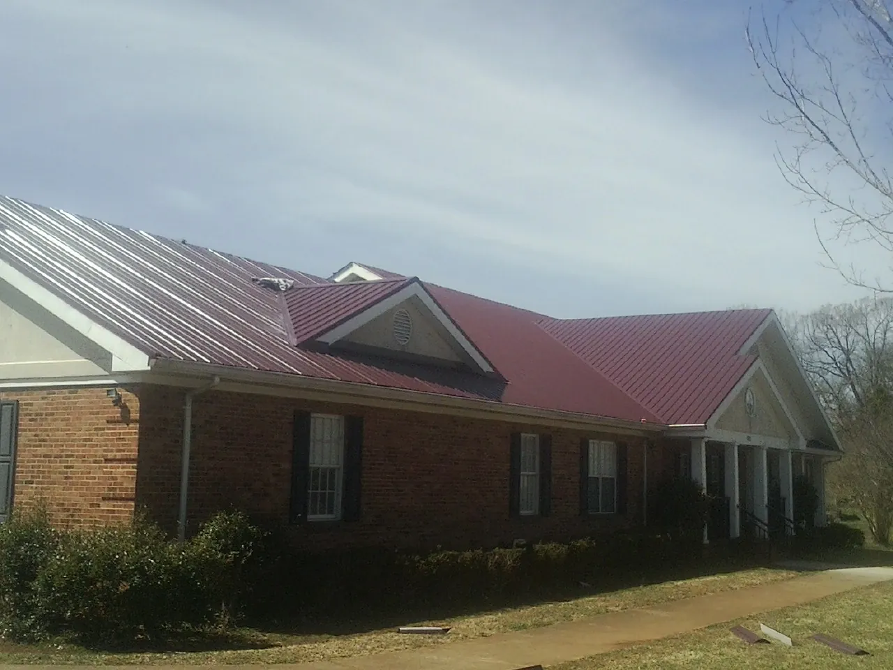 Red metal roof with gabled entries on a long brick building, from a Hail Damage Roof Repair job in Westerlo