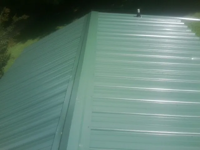 New green metal panels meeting at the ridge of a roof — Flat Roof Repair work by our crew in Westerlo