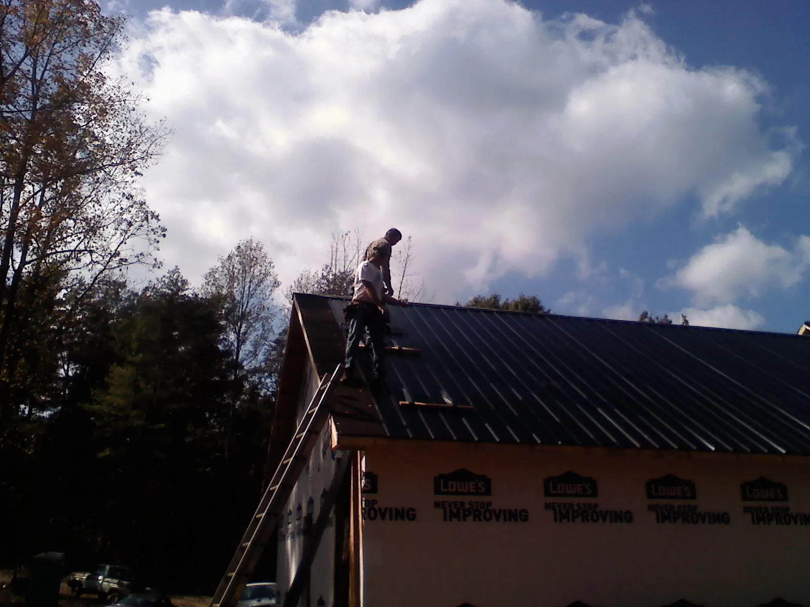 Roofer fastening dark metal panels high against a cloudy sky, from a Roof Inspection job in Westerlo